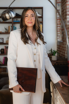 Woman in a white blazer holding a brown portfolio in a stylish home office.