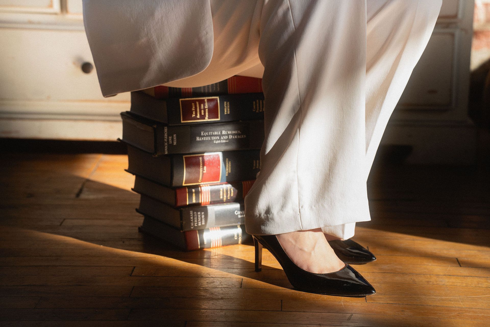 Woman’s black heels propped on a stack of books, under a white blanket on a wooden floor