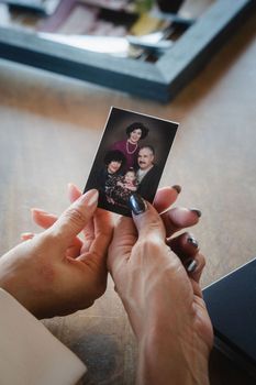 Hands holding a small family photo over a couch in a softly lit room
