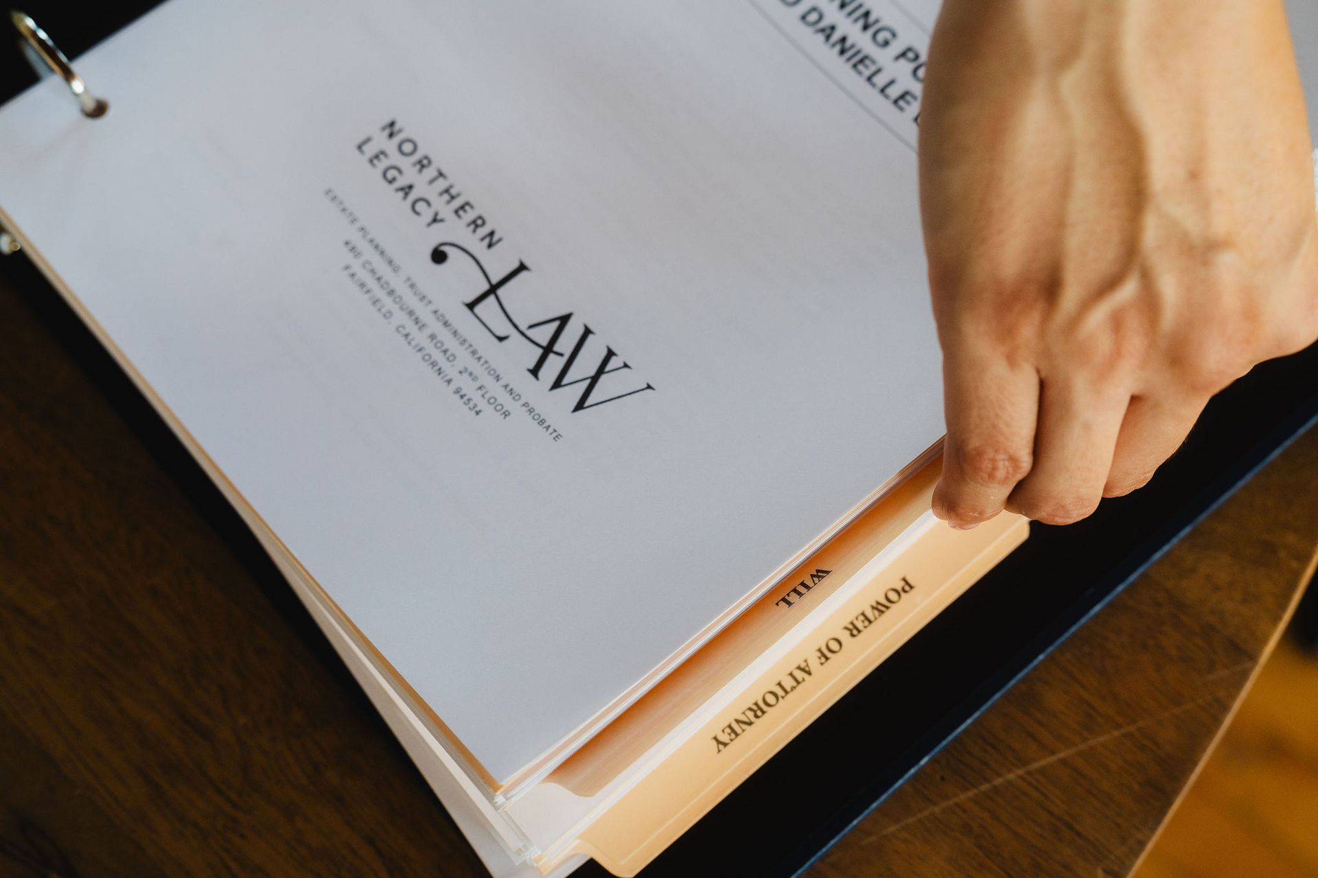 Hand opening a binder labeled “Law,” with a stack of papers on a wooden desk.