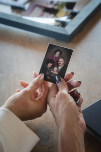 Hands holding a small family photo over a wooden table with a blurred photo frame in the background