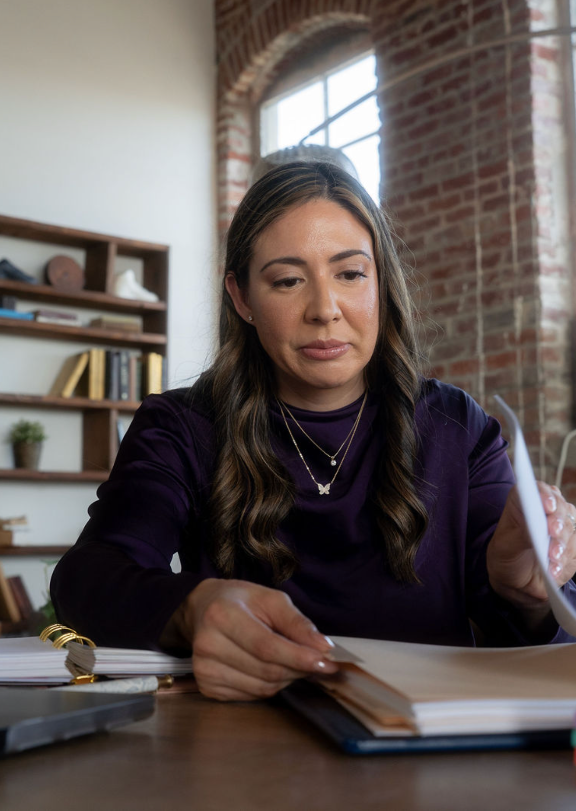 Woman sitting at a desk with a notebook and pen in a bright office, looking down thoughtfully