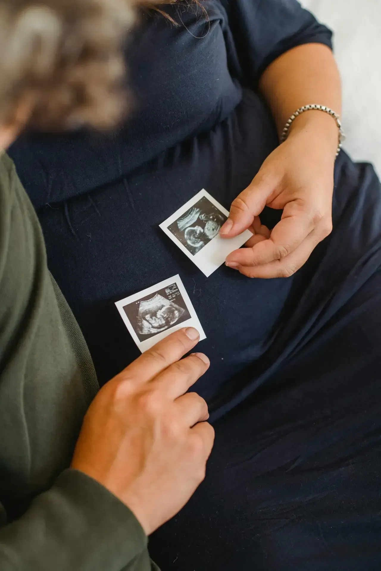 Two people hold ultrasound printouts on a couch, one in navy and one in green.
