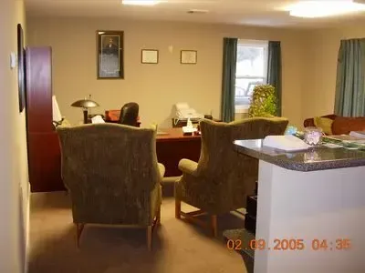Office with two armchairs facing a desk, window with blue curtains, file cabinet, dated look.