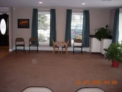 Empty room with brown carpet, two windows with teal curtains, and a small table and chairs.