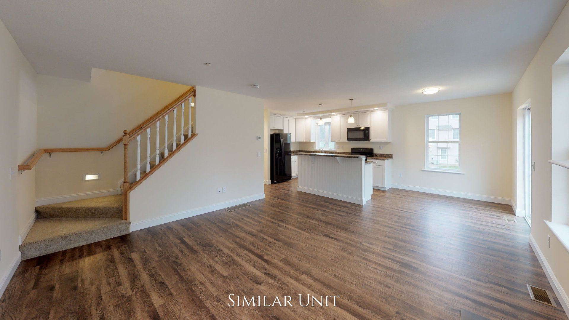 An empty living room with hardwood floors and stairs leading to the kitchen.