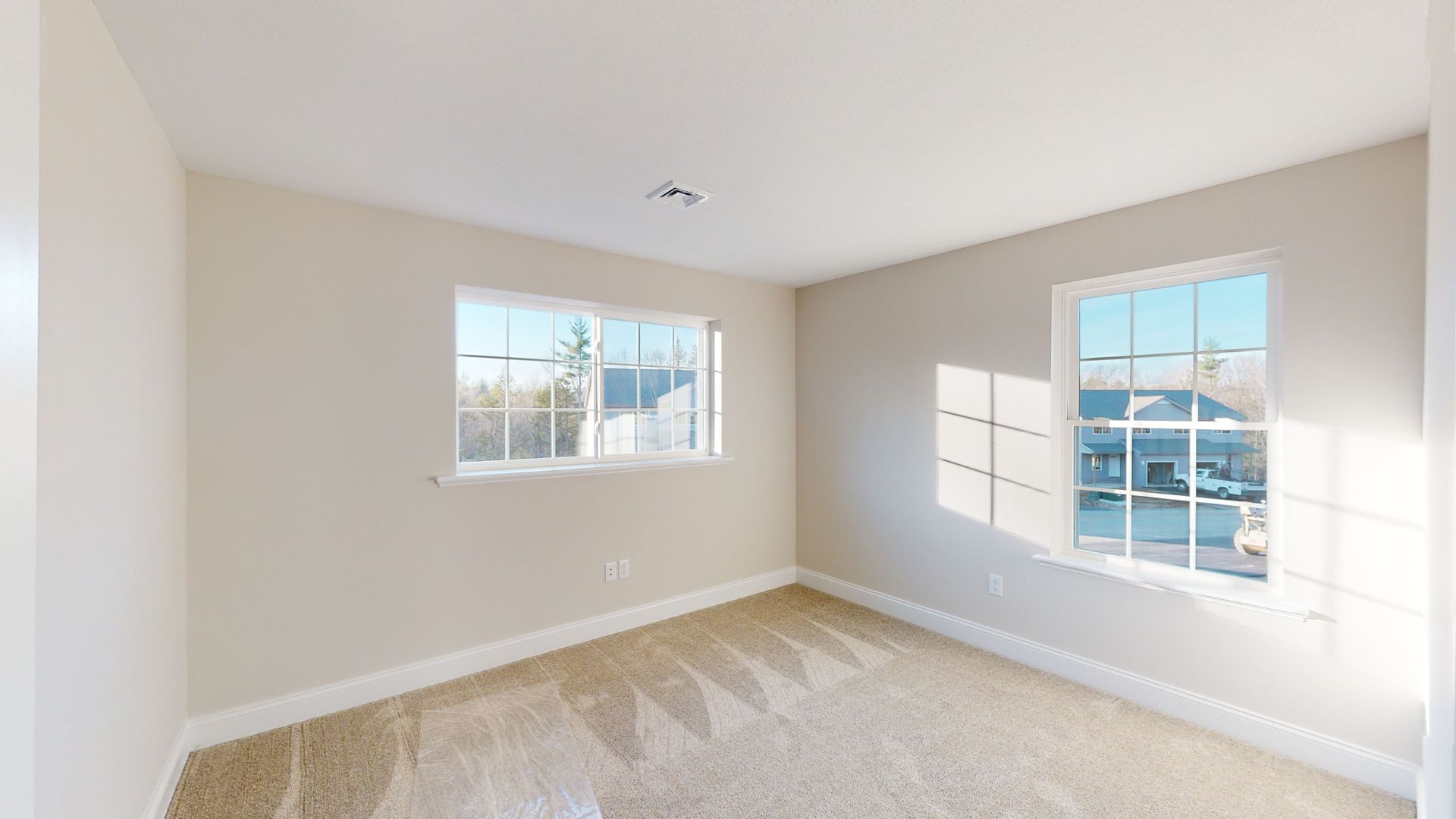 An empty bedroom with two windows and a carpeted floor.
