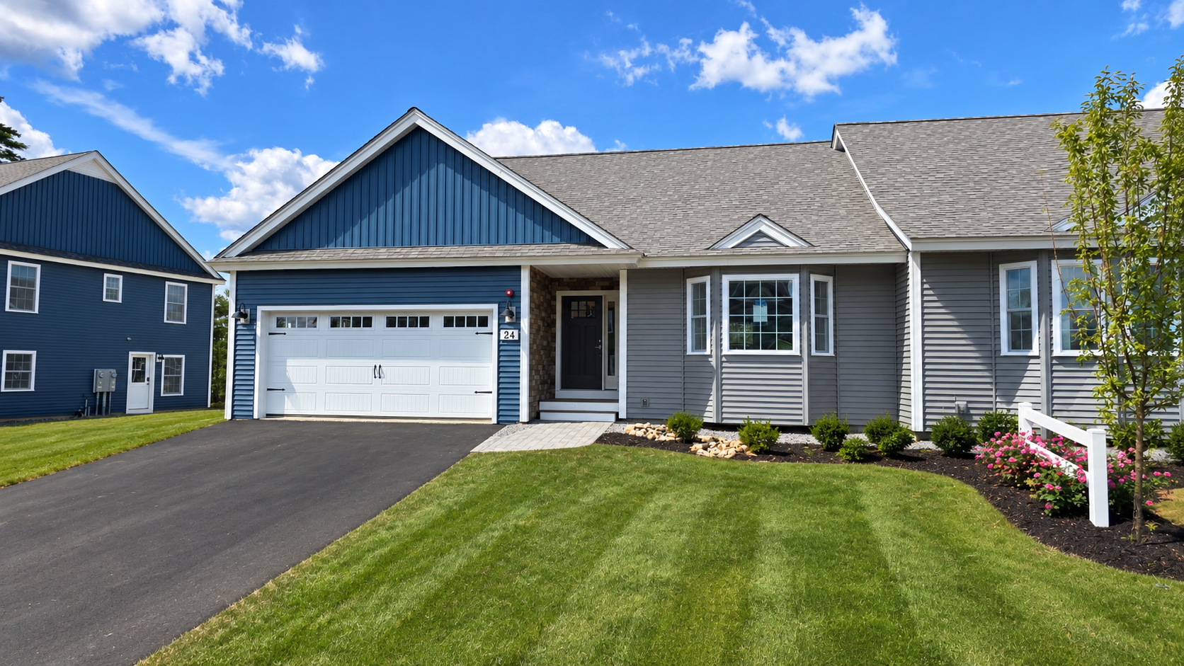 Single-story gray house with blue gables, white garage, and a manicured lawn under a blue sky.