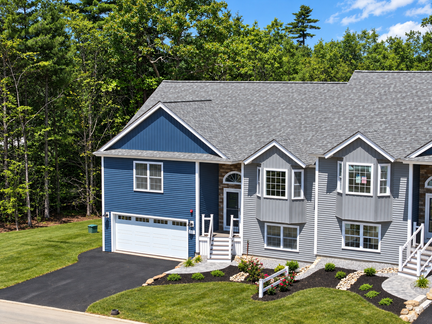 Blue and gray suburban house with garage, driveway, and landscaped front yard beside trees