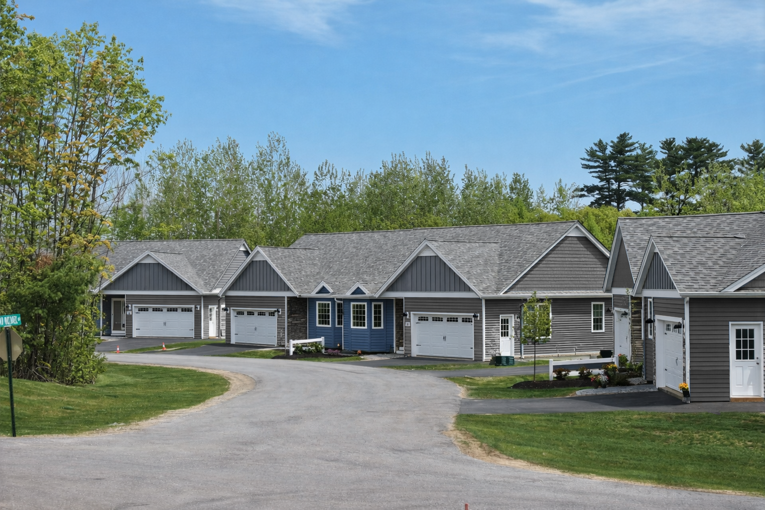 Row of gray-roofed suburban homes along a curved paved driveway under a blue sky