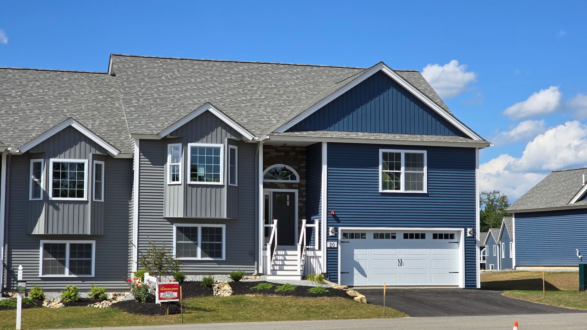 Blue-gray suburban house with white trim, front porch, and two-car garage under a bright sky