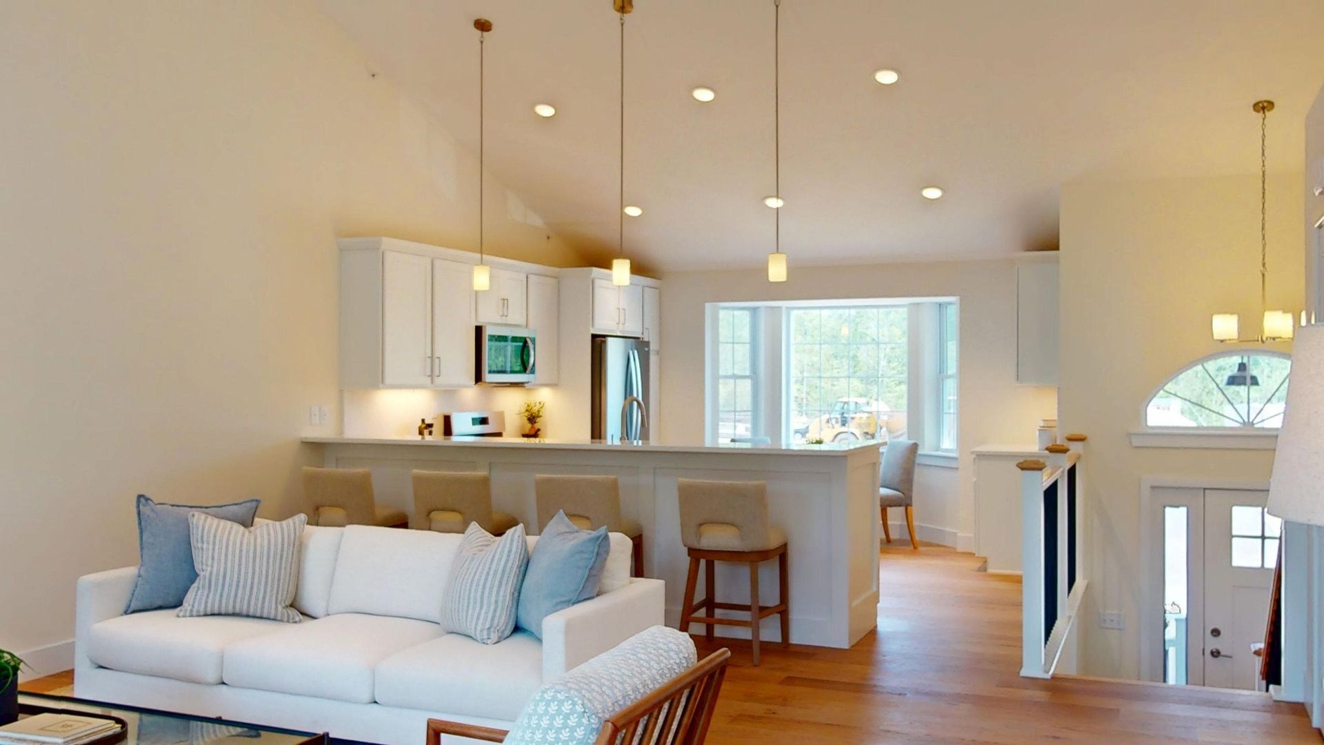 Bright open living room with white sofa, blue pillows, kitchen island, and wood floors
