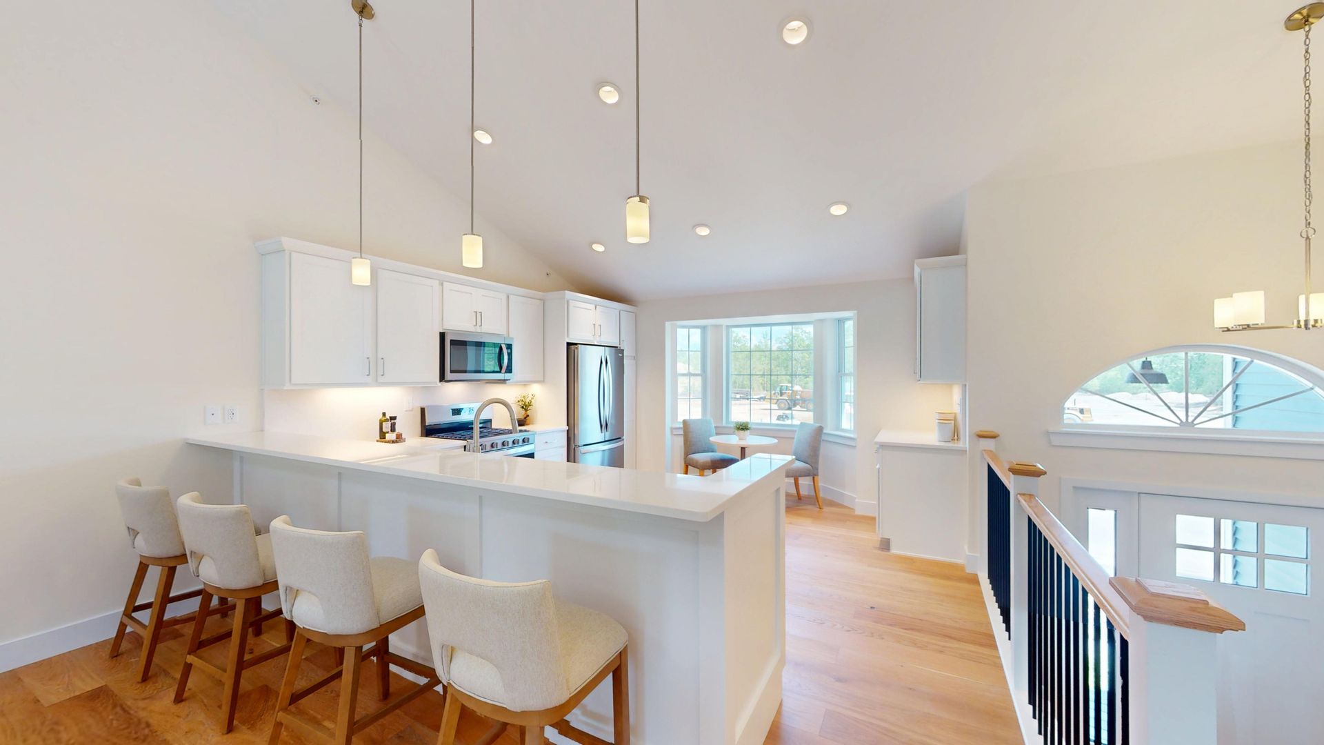 Bright modern kitchen with white island, pendant lights, bar stools, and open view to a staircase and windows
