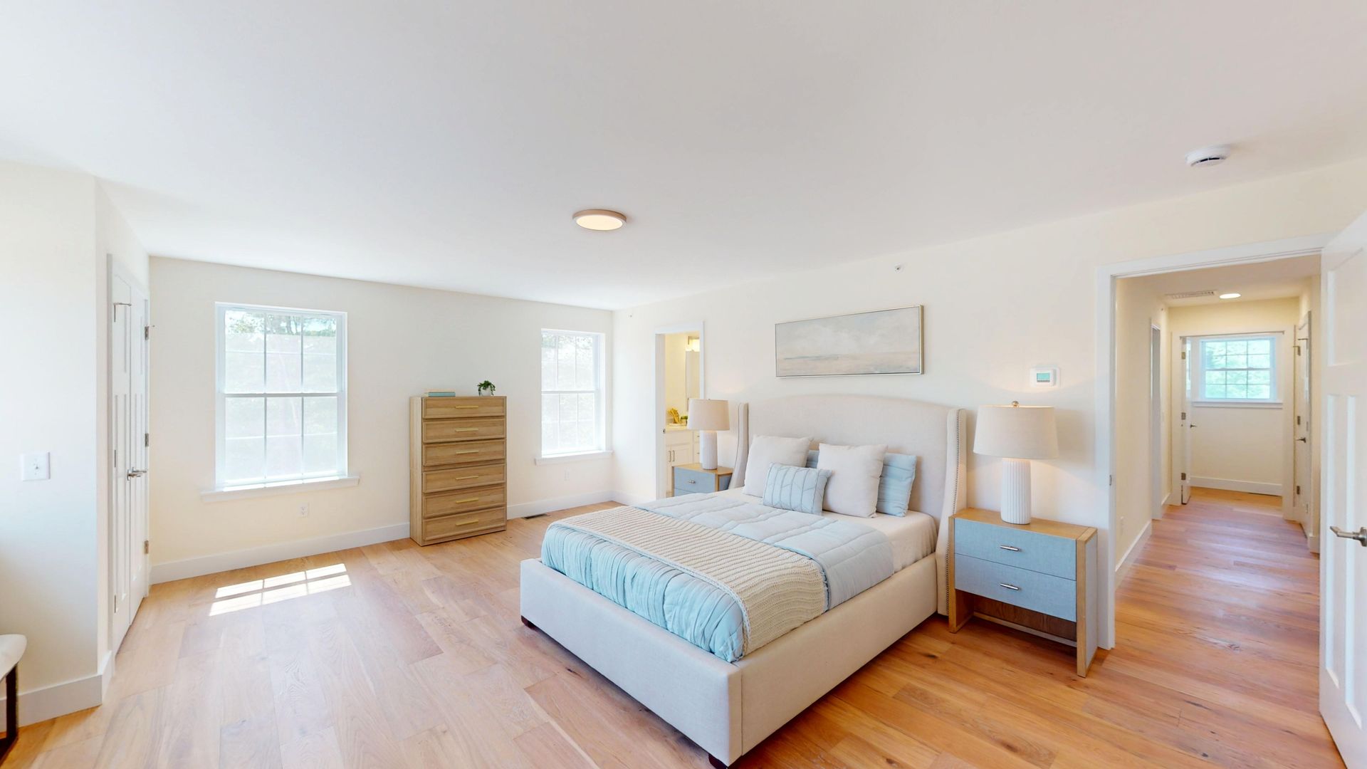Bright bedroom with a bed, dresser, nightstand, and hardwood floors in a minimalist white room