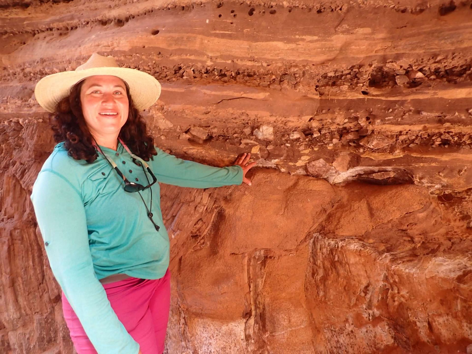 A woman wearing a cowboy hat is standing in front of a rock wall