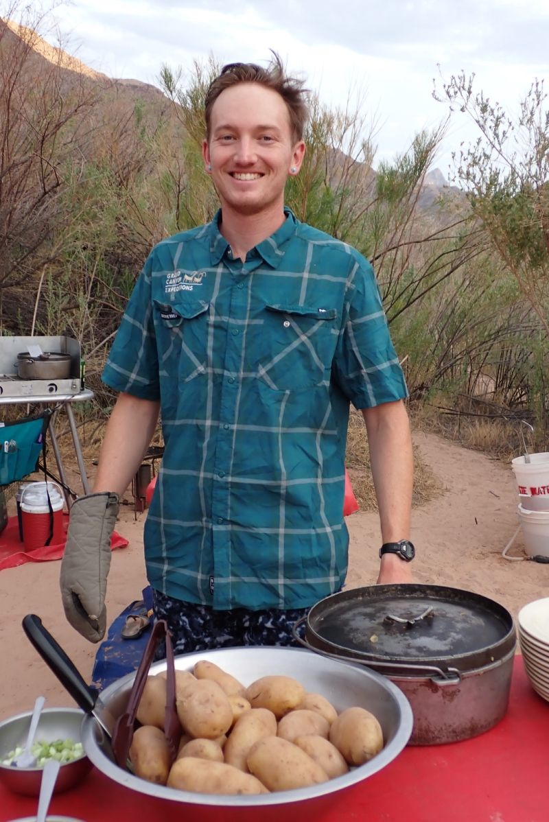 A man in a plaid shirt is standing next to a bowl of potatoes.