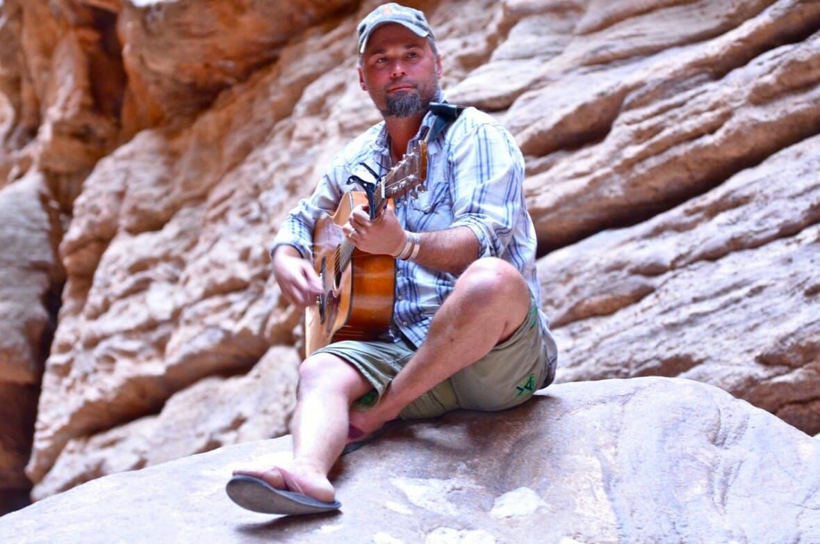 A man is sitting on a rock playing a guitar