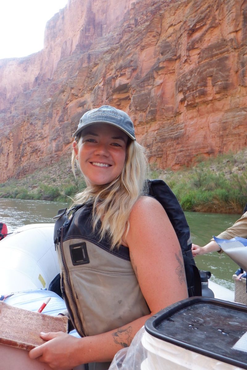 A woman is smiling while sitting on a raft on a river.