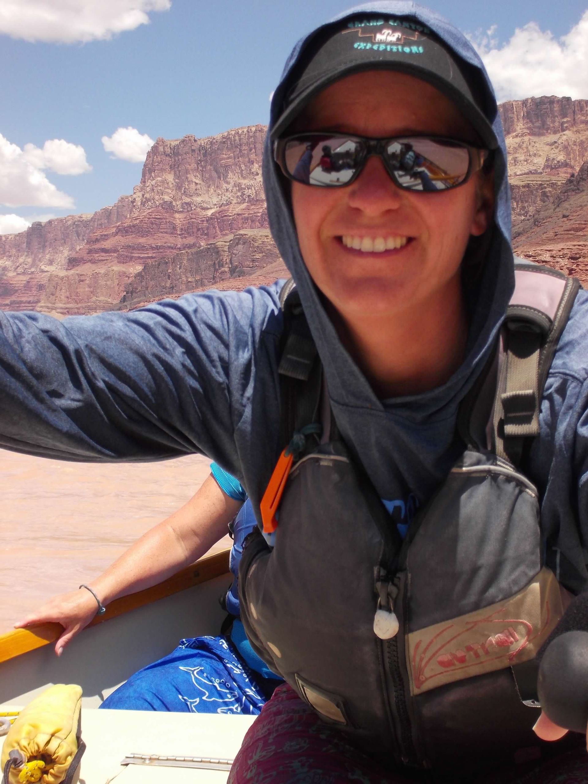 A person wearing a hooded jacket and sunglasses is smiling for the camera
