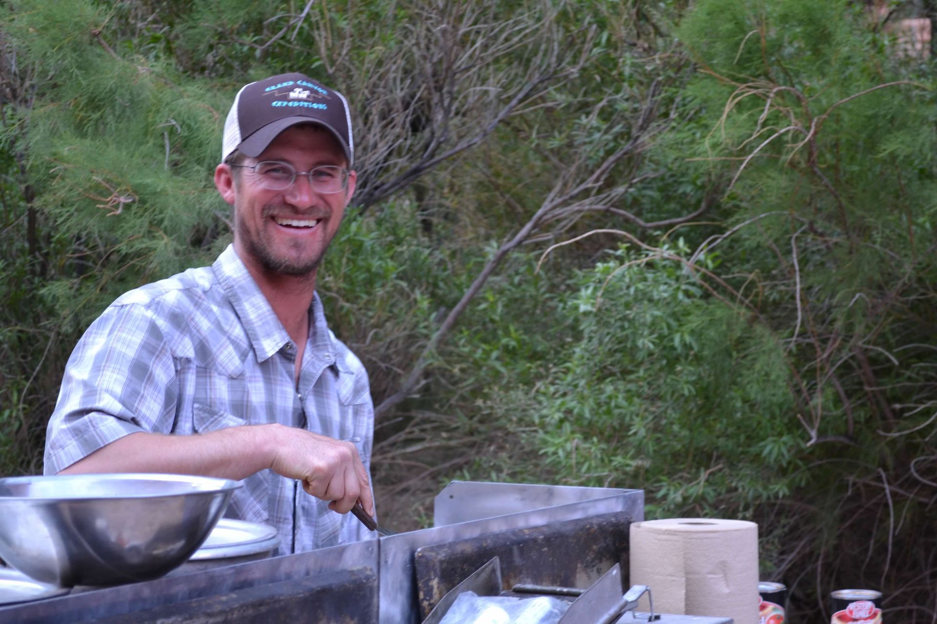 A man wearing a hat and glasses is smiling while cooking