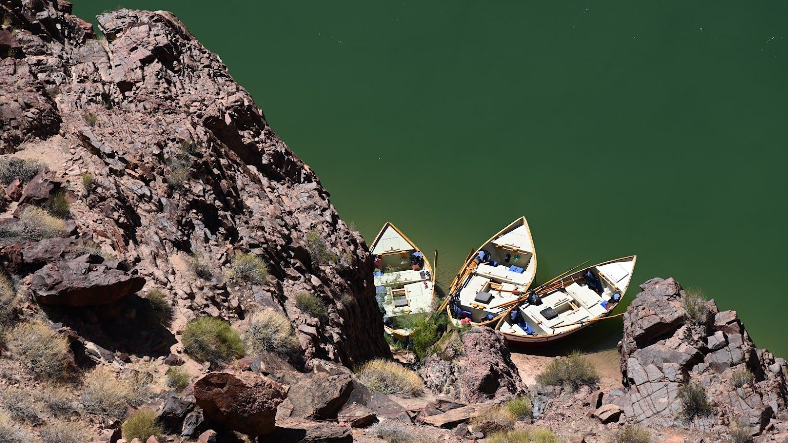 Three boats are sitting on a rocky cliff near a body of water