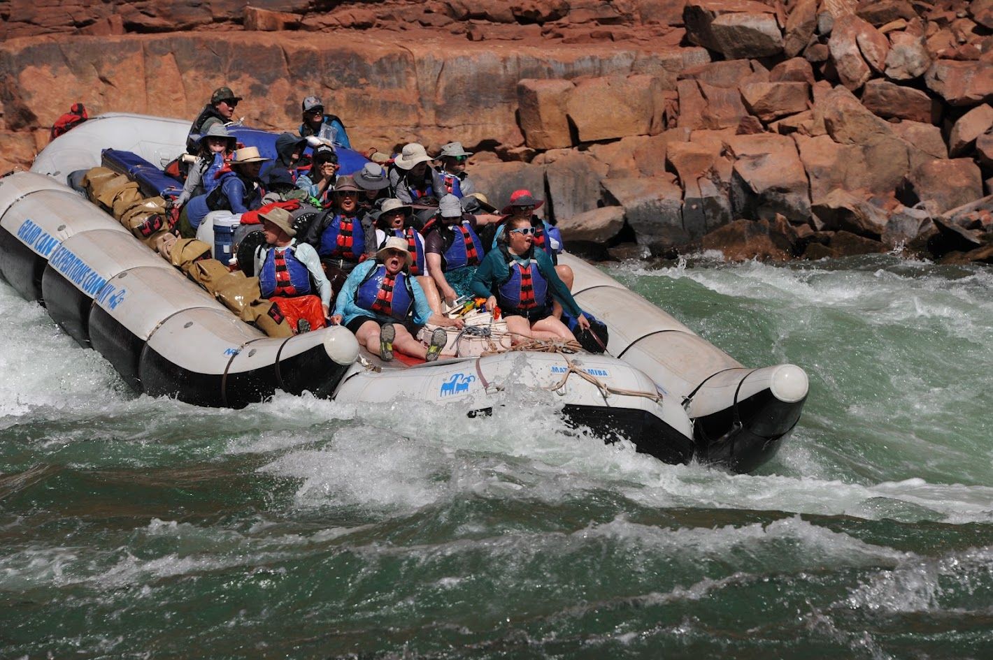 A group of people are rafting down a river in a boat that says water adventures