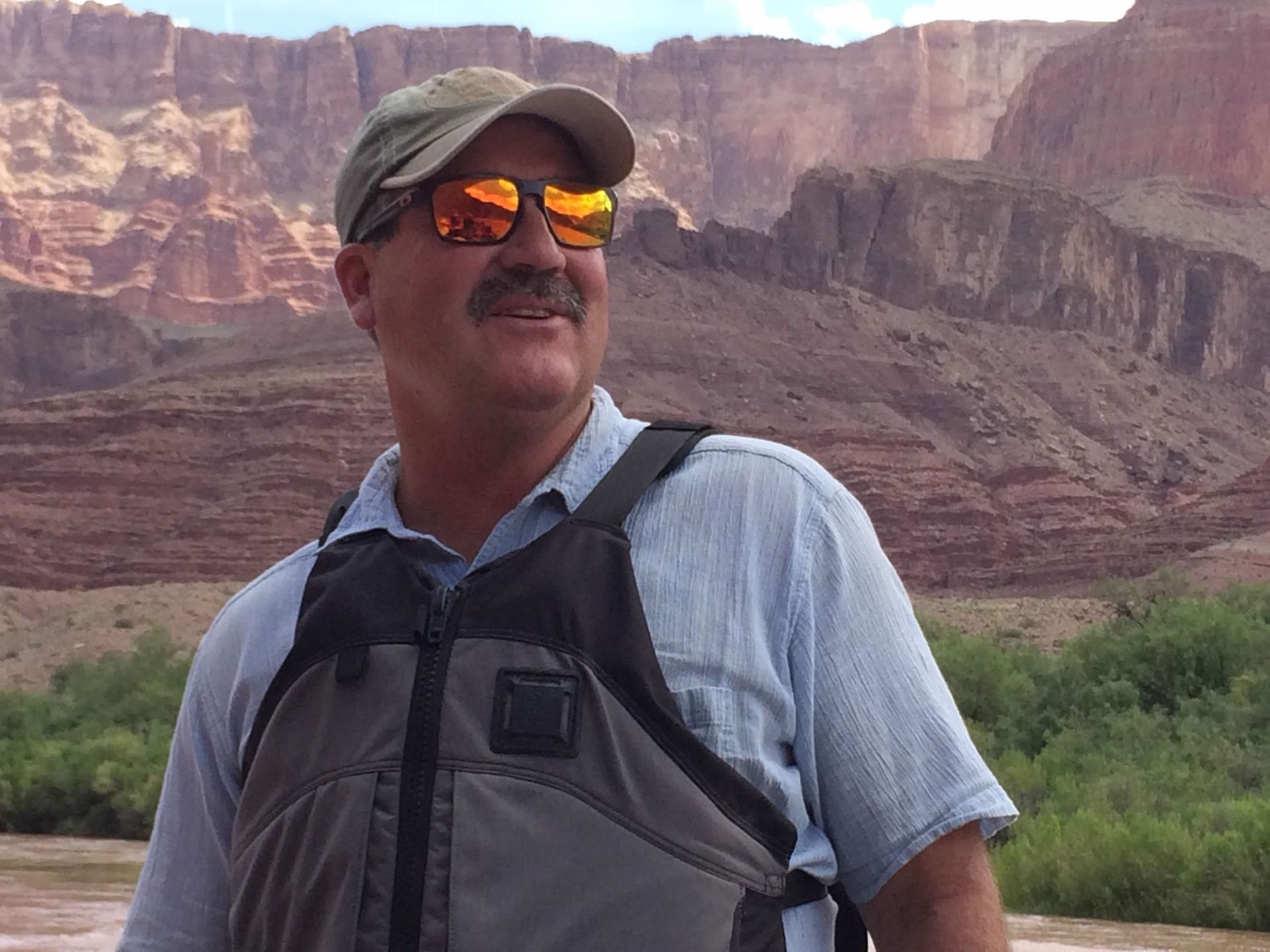A man is standing next to a raft in the water holding a paddle and giving a thumbs up.