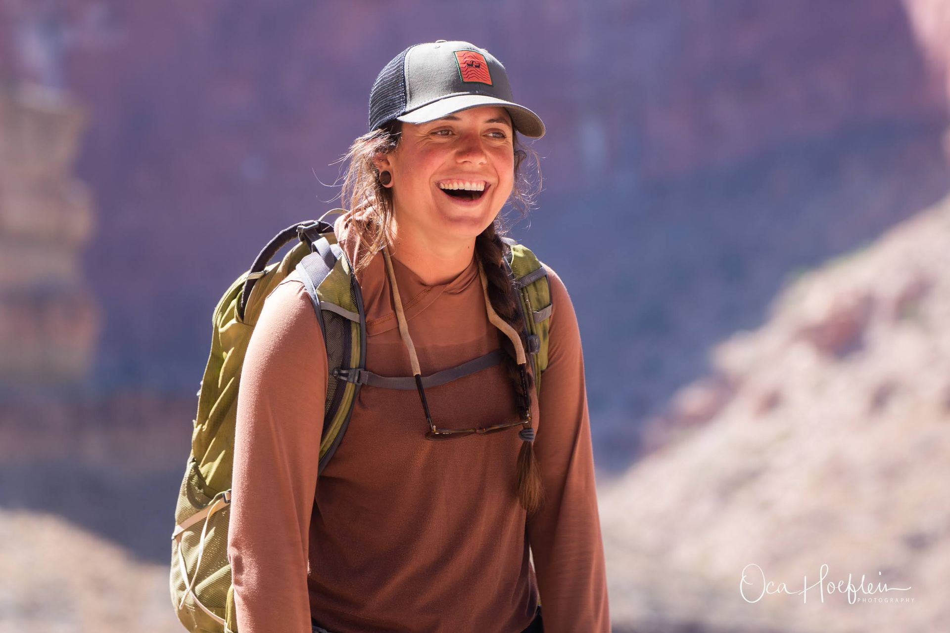 A woman wearing a hat and a backpack is smiling.