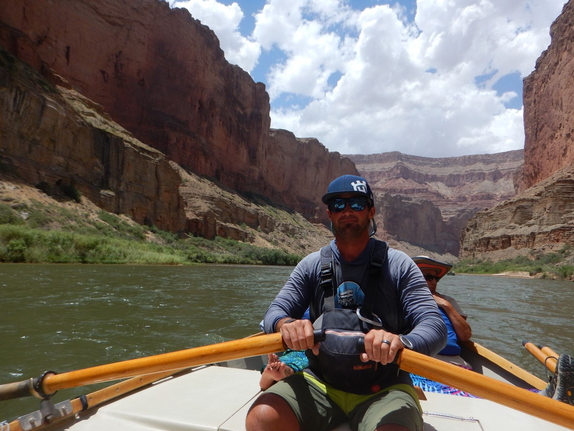 A man is rowing a boat down a river with mountains in the background.