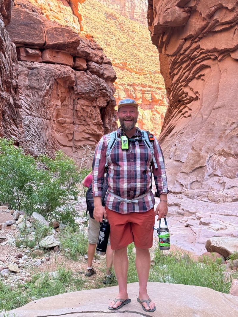 A man in a plaid shirt is standing in a canyon holding a lantern.