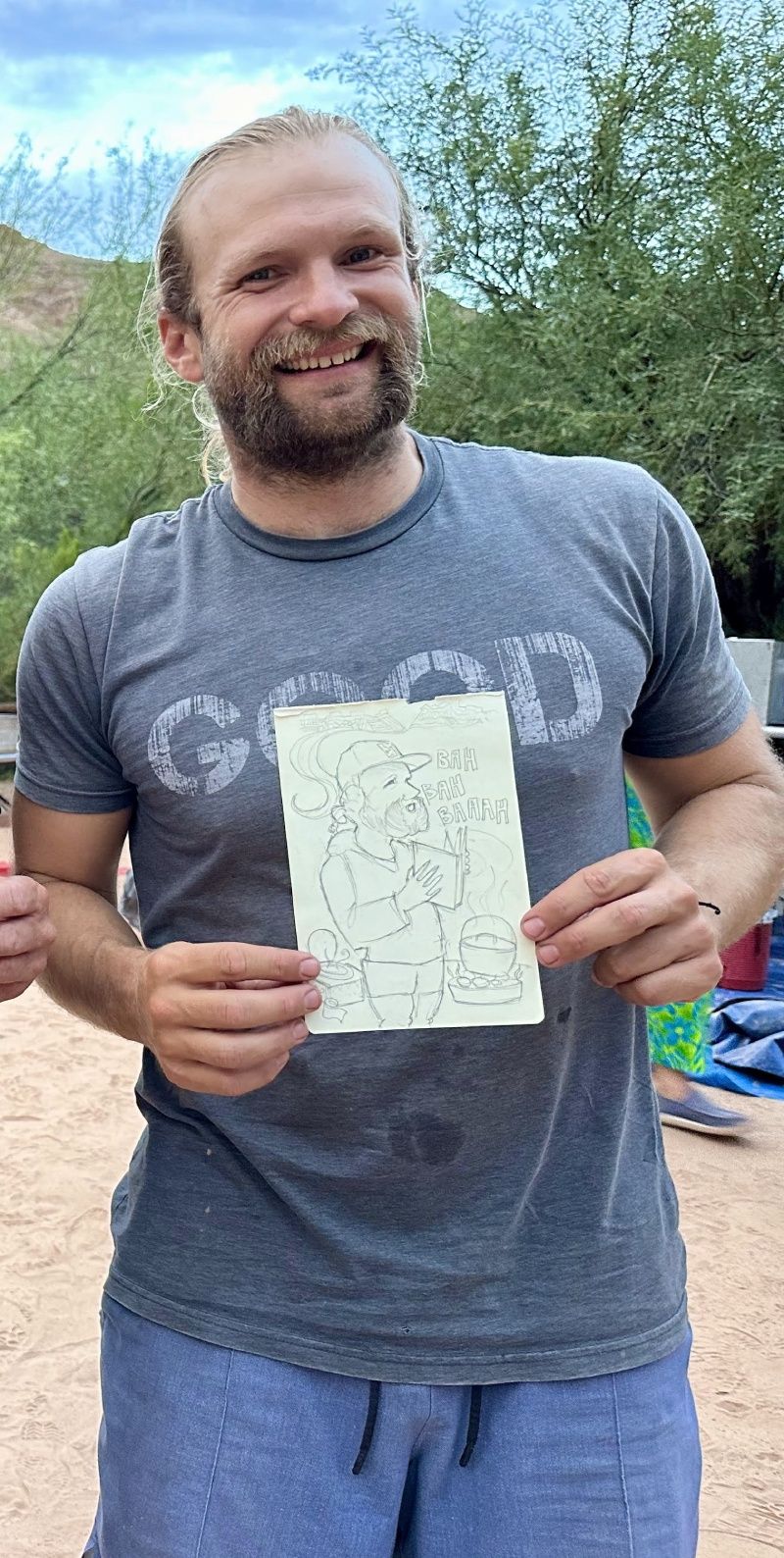 A man in a gray shirt is holding a piece of paper with a drawing on it.