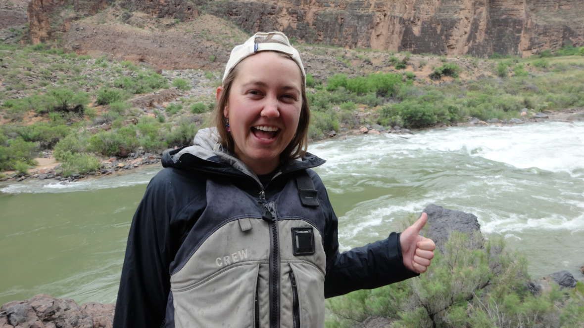 A woman is giving a thumbs up in front of a river.