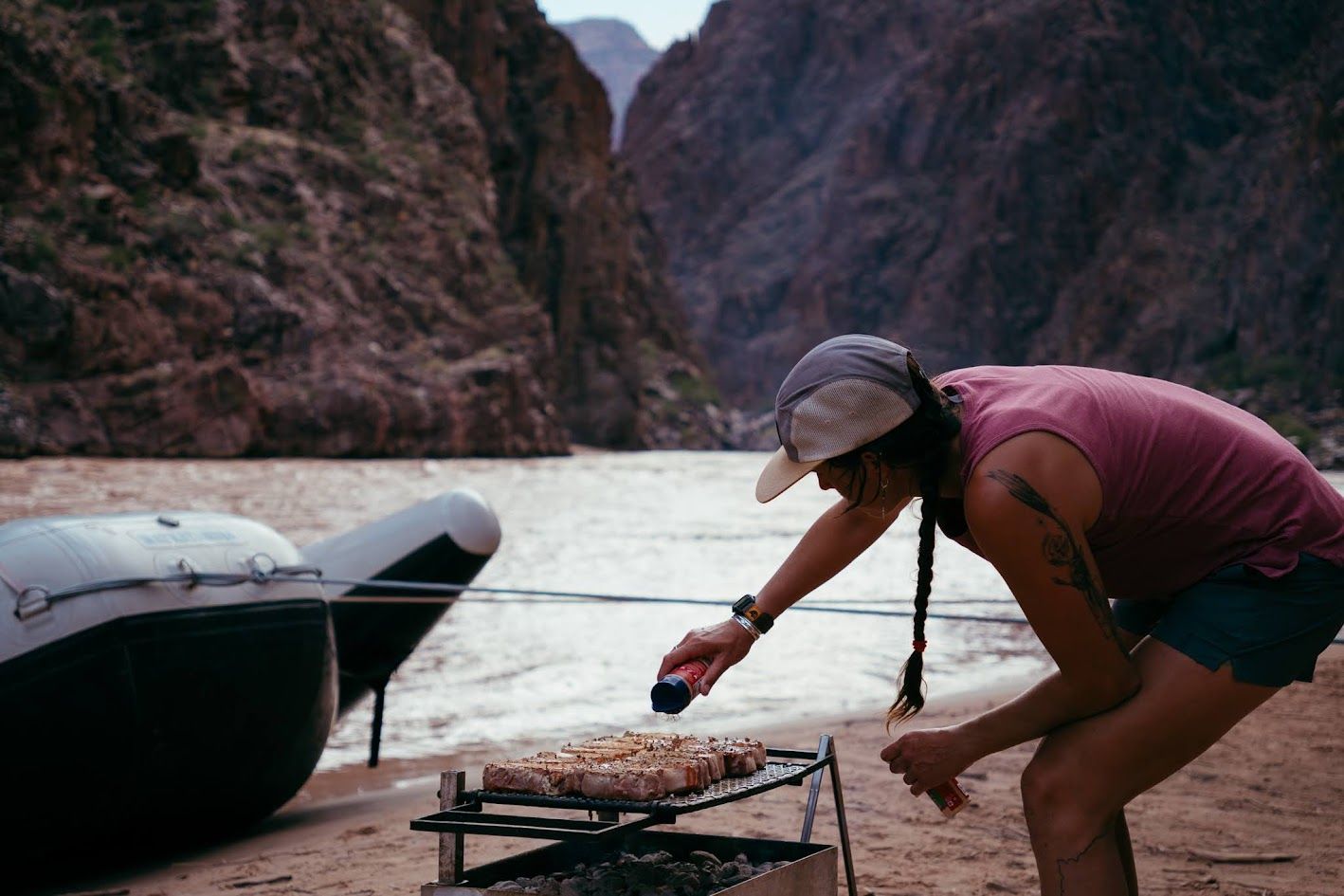 A woman is grilling food on the beach near a river
