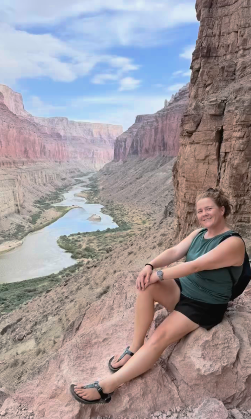 A woman is sitting on a rock overlooking a river.