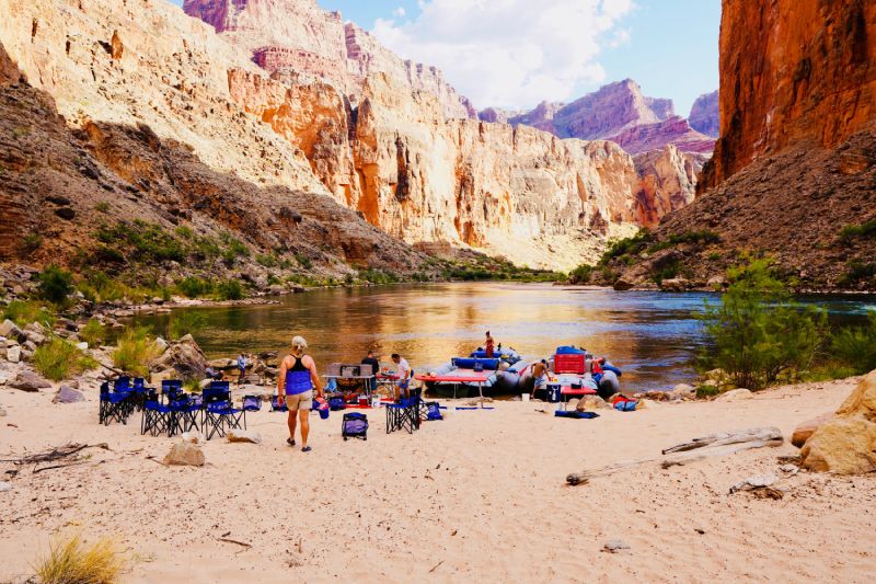 A group of people standing on a sandy beach near a river