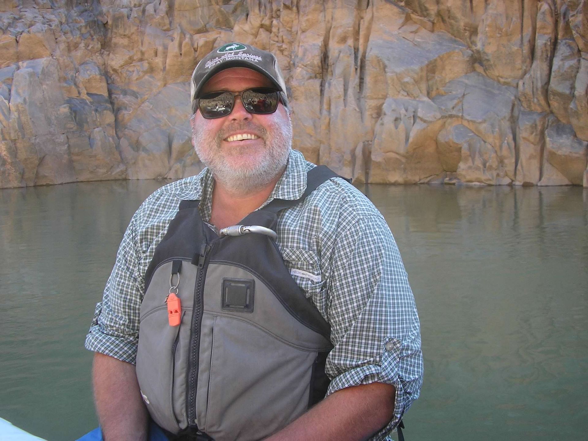 A man in a plaid shirt is sitting on a rock in the grass