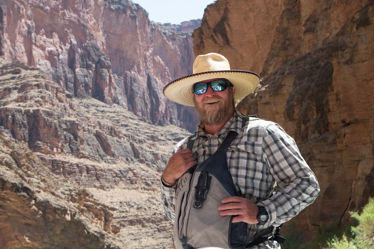 A man wearing a hat and sunglasses is standing in front of a canyon.
