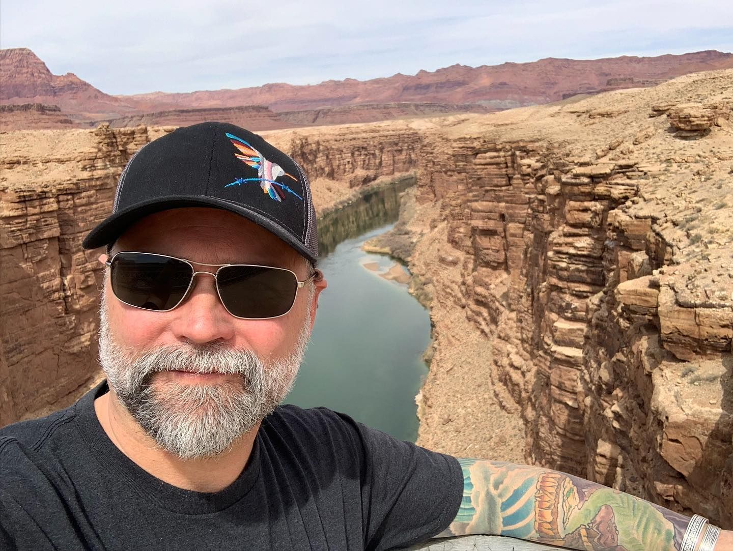 A man with a beard and sunglasses is standing in front of a river.