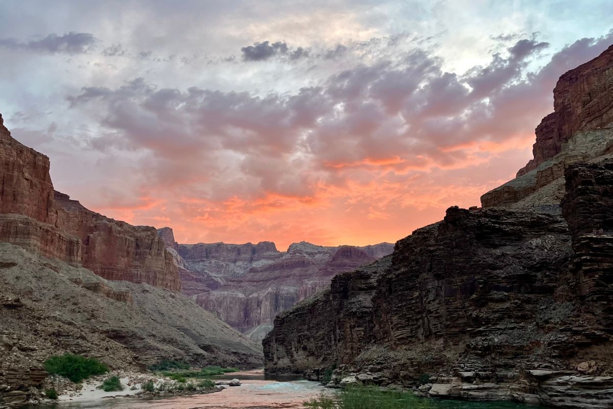 Sunset over a canyon river, with red and orange sky, and towering rock walls.