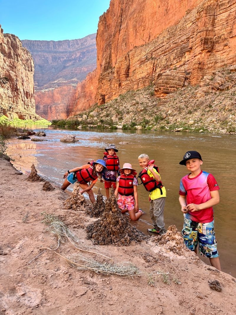 A group of children wearing life jackets are standing next to a river