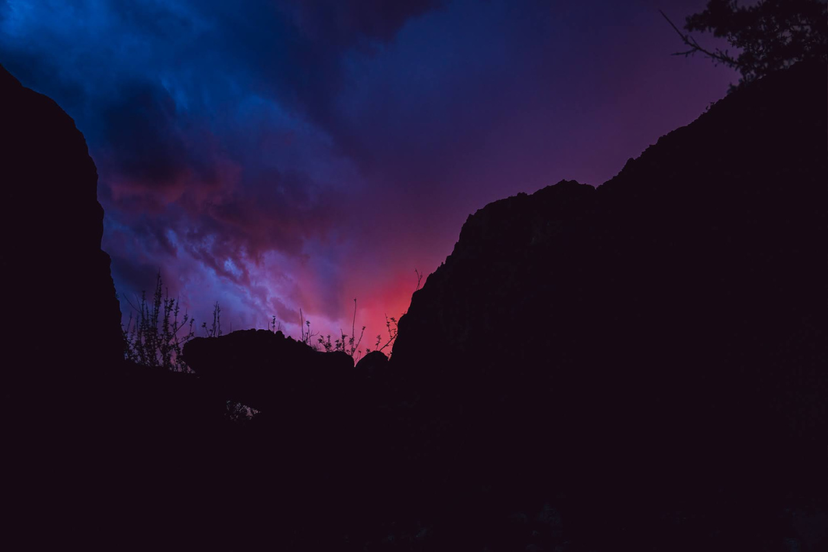 A sunset over a canyon with trees in the foreground and a purple sky in the background.