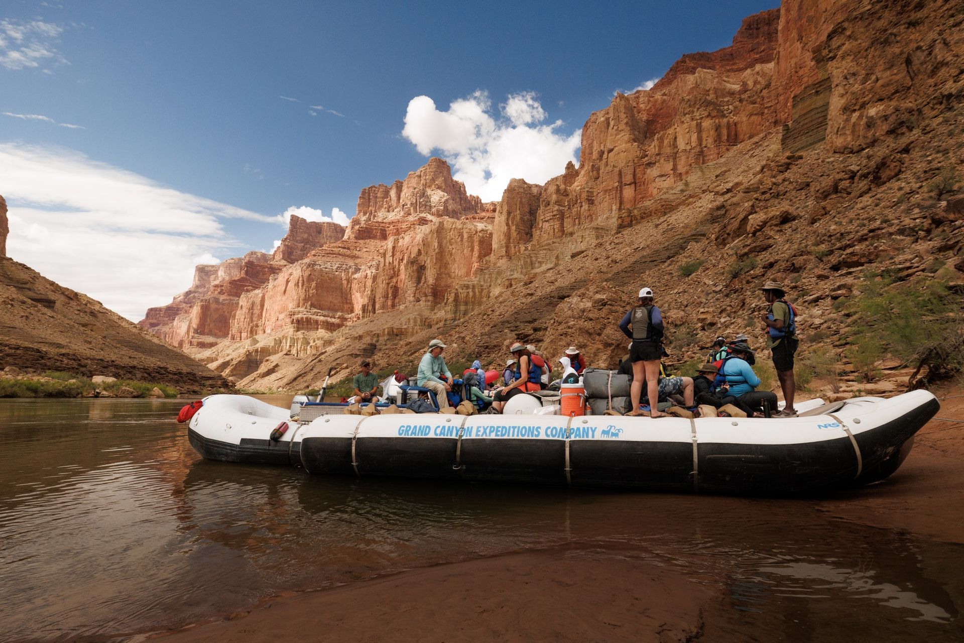 A raft of guests on the Colorado River beside towering red rock canyon walls