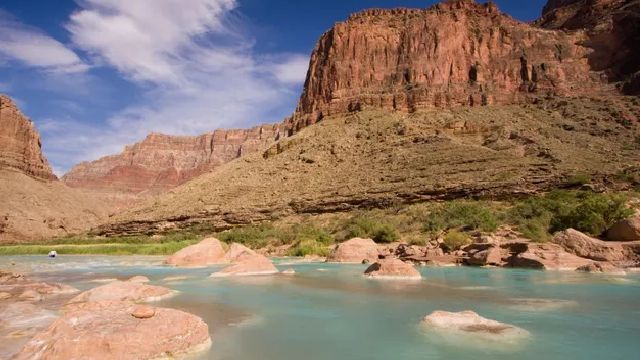 A river in the middle of a canyon with mountains in the background