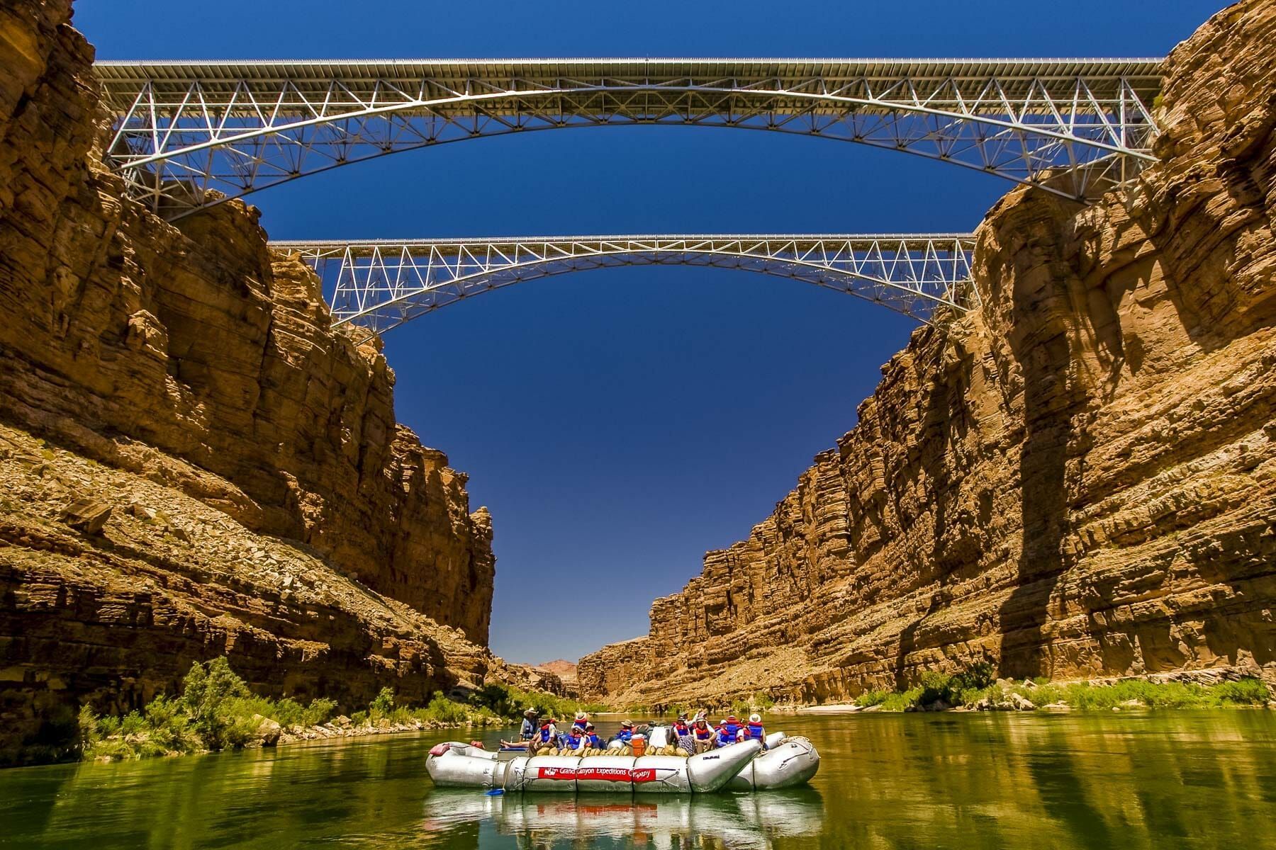 A group of people are rafting down a river under a bridge.
