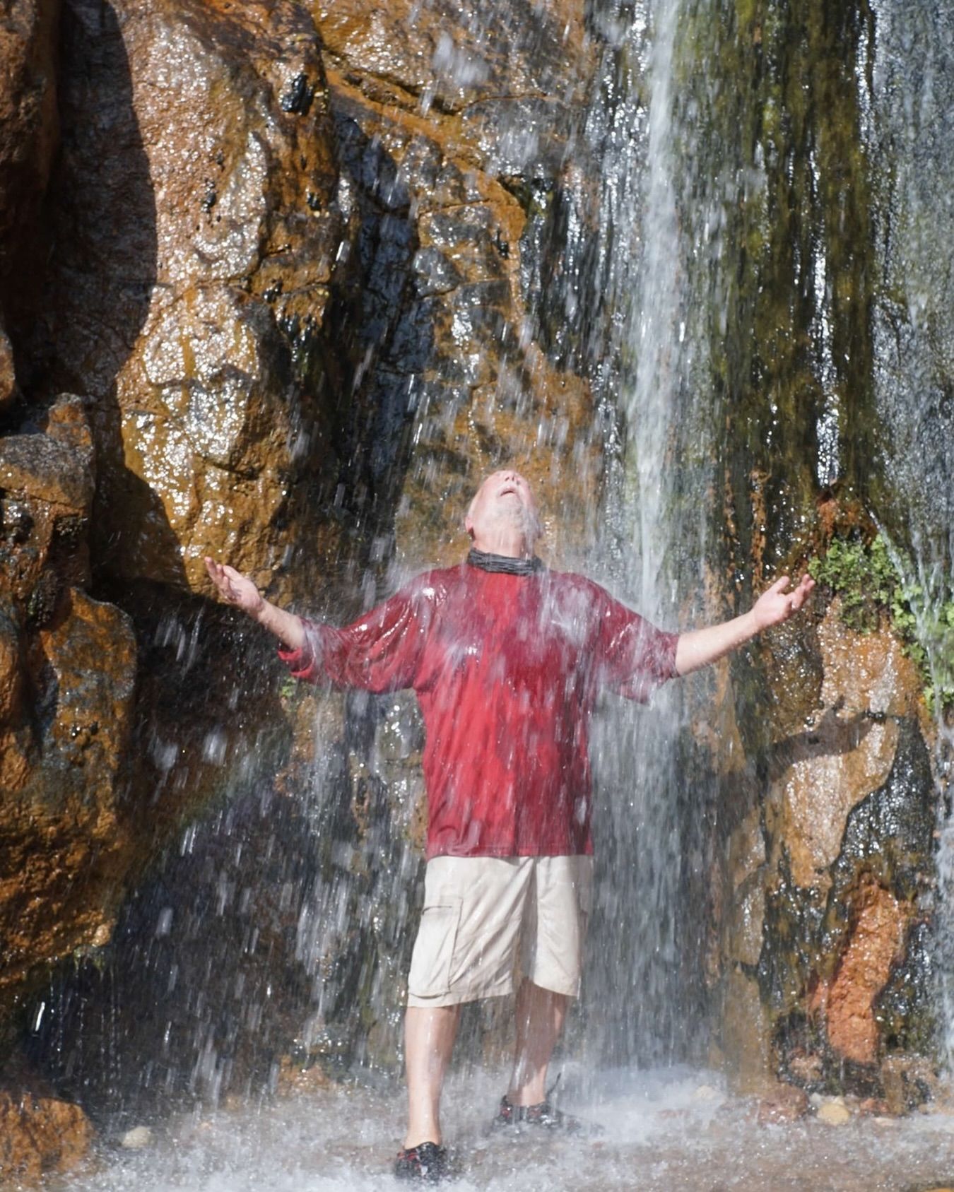 A man in a red shirt is standing under a waterfall