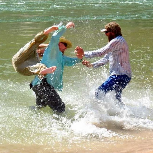 A man in a cowboy hat is standing in the water with two other men