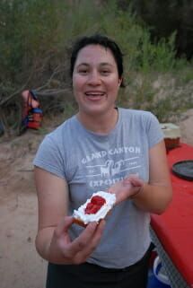A woman in a grey shirt is holding a piece of cake with strawberry jam on it.