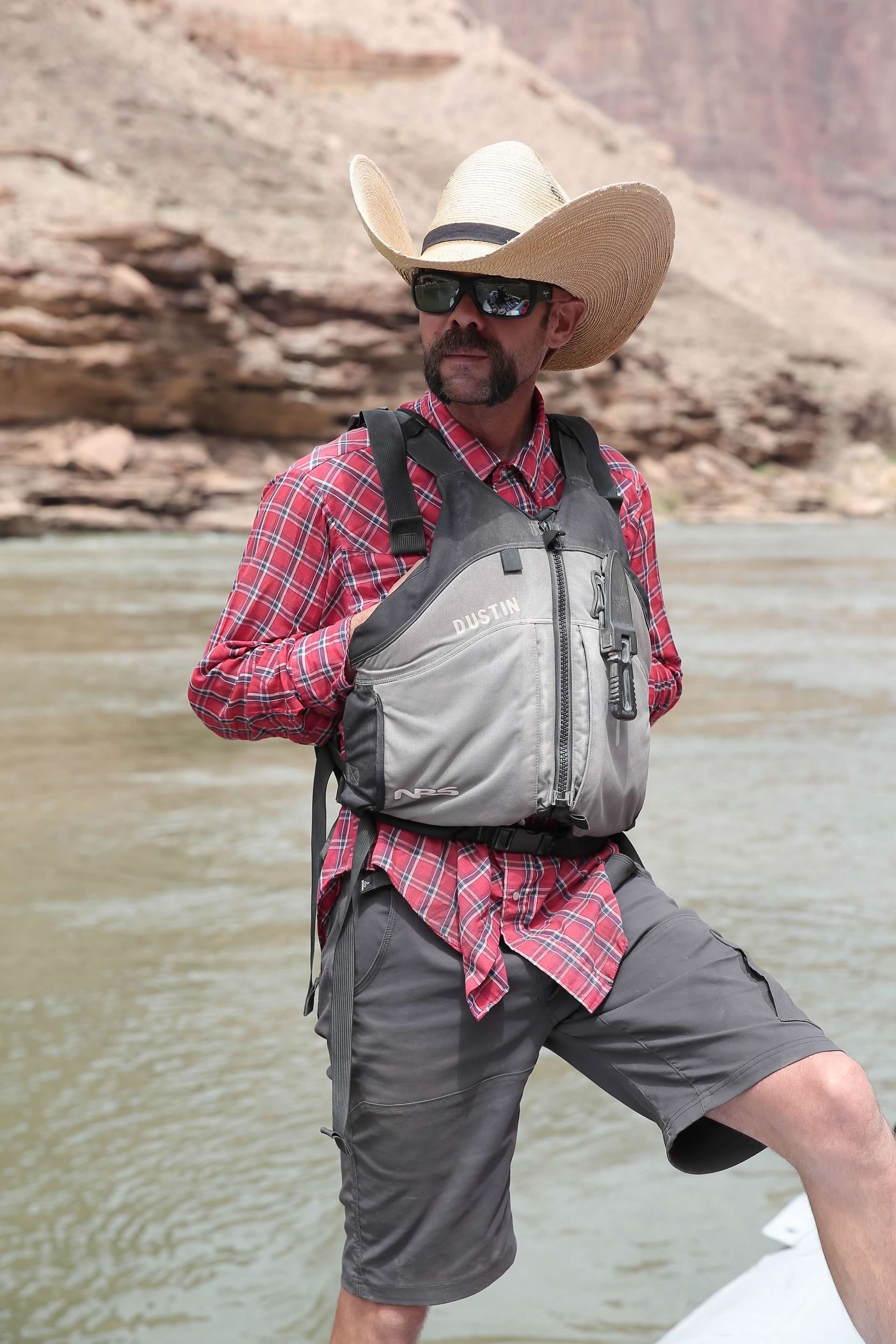 A man wearing a cowboy hat and sunglasses is standing on a boat in the water.
