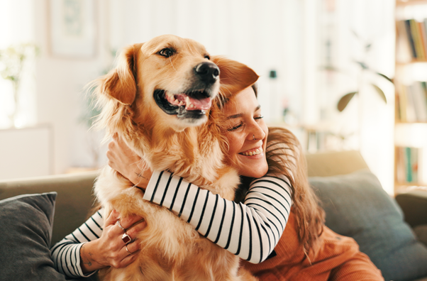 Woman hugging golden retriever on a couch in a bright living room