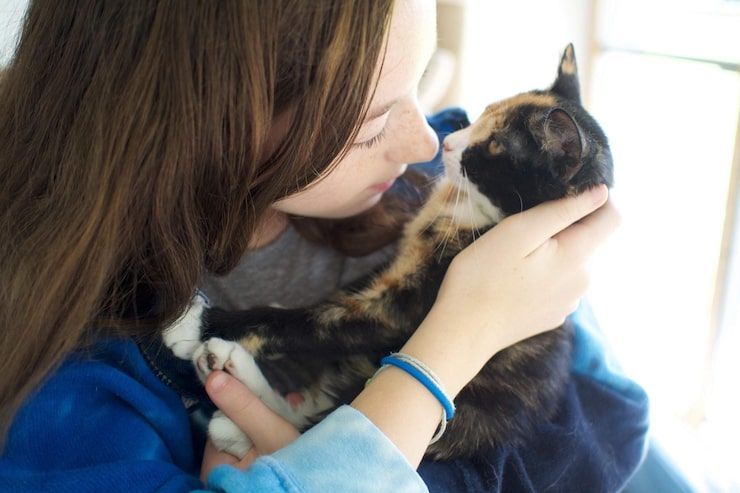 Woman holding a tortoiseshell cat close to her face in a bright room